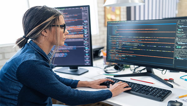 Vrouw programmeert achter twee computerschermen