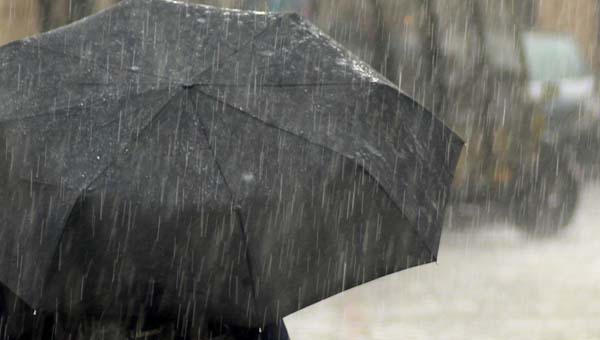 Persoon met rug naar de camera staat in de regen onder een paraplu