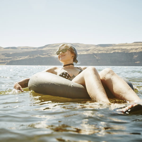 Vrouw in badkleding ligt relaxed op het water in een zwemband dankzij reisverzekering van Aon