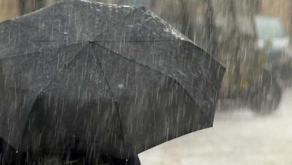 Persoon met rug naar de camera staat in de regen onder een paraplu